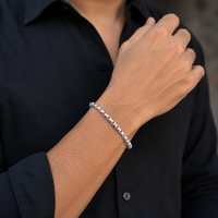 A close-up of a person's wrist wearing a silver-toned chain link bracelet, shown against a black button-down shirt.